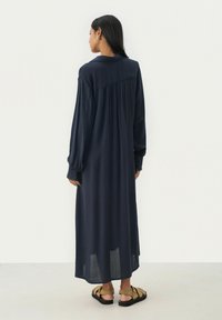 Marineblaues, langärmliges Kleid mit einem gefalteten Rückendesign, aus leichtem Stoff gefertigt, mit umgeschlagenen Ärmeln und einer fließenden Silhouette.