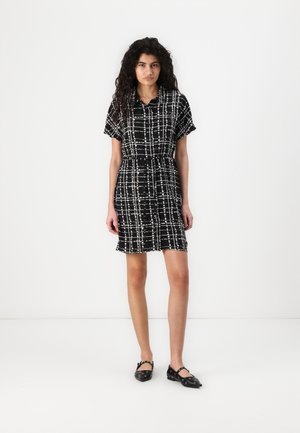 Robe noire et blanche à manches courtes avec un motif à carreaux, ceinture à la taille et coupe au genou. Associée à des ballerines noires et à un design minimaliste.