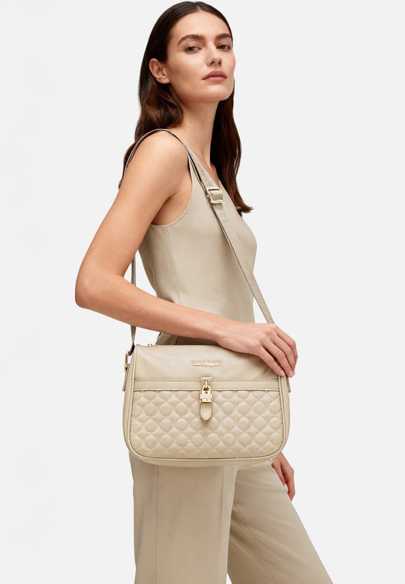 Borsa a spalla trapuntata color beige con dettagli in oro. Caratterizzata da una chiusura a pattina e una tracolla regolabile. Tessitura liscia e forma strutturata.