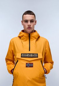 Yellow waterproof jacket with a front pocket featuring a logo and Norwegian flag. Has a zip closure and cinched cuffs for a secure fit.