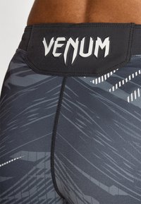 Calções de desporto pretos com um tecido suave e elástico, adornados com um padrão abstrato cinza-escuro. A cintura tem um logo branco "VENUM".