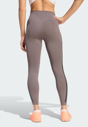 High-waisted, taupe leggings with a smooth texture, featuring black side stripes and a seam detail on the back. Paired with bright sneakers.