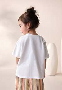 Fehér, rövid ujjú, puha anyagból készült póló, színes csíkos nadrággal párosítva, laza szabással és egyszerű nyakkivágással.