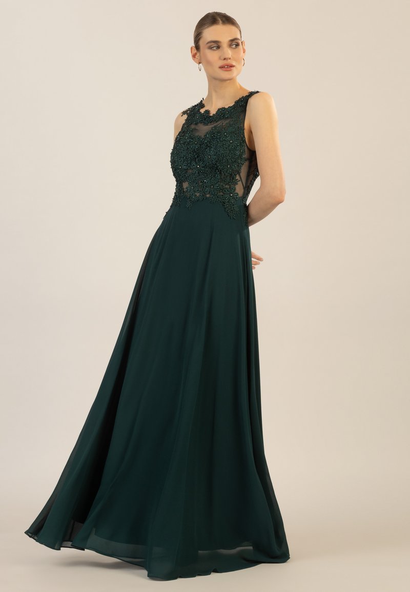 Langes smaragdgrünes Kleid mit einem taillierten Oberteil, das mit floraler Stickerei und transparenten Einsätzen verziert ist, fließender Rock mit einer vollen Silhouette und glatter Textur.