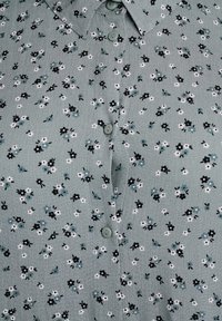 Green floral blouse featuring a pattern of small black, white, and blue flowers. Includes a button-up front and a collar. Soft texture.