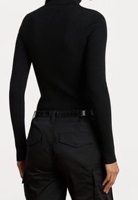 Černý žebrovaný rolák se štíhlým střihem, v kombinaci s černými cargo kalhotami s lesklým páskem a kapsami na zadní straně.