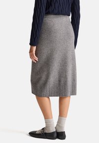 Šedá pletená midi sukně s žebrovaným lemem, vyrobená z měkké látky. Spárována s černými plochými botami a šedými texturovanými ponožkami.