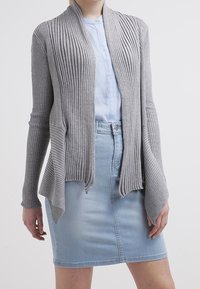 Cardigan grigio a coste con apertura frontale e maniche lunghe, indossato su una camicia azzurro chiaro con bottoni e una gonna a matita in denim.