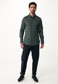 Camicia a quadri verde con bottoni, realizzata in tessuto, abbinata a pantaloni cargo scuri e scarpe da ginnastica nere con dettagli bianchi.