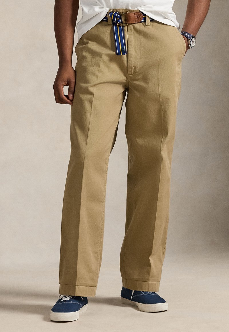 Μπεζ βαμβακερό παντελόνι με ίσια γ ραμμή, διακοσμημένο με καφέ δερμάτινη ζώνη που έχει μπλε και κίτρινες ρίγες και λεπτομέρεια με λογότυπο.