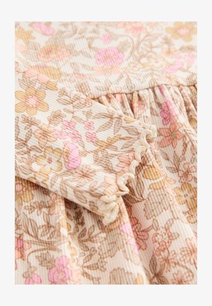 Tissu à motif floral en beige clair avec des fleurs roses et brunes. Présente une texture côtelée et des bords délicatement volantés sur les manches.