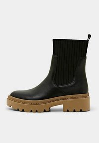 Bottines noires avec une tige en tissu côtelé et une semelle épaisse beige. Extérieur en cuir lisse et tirant pour un enfilage facile.
