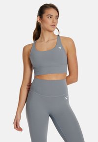 Sostenedor deportivo gris y leggings de tiro alto a juego, fabricados con un tejido suave, que presentan un diseño minimalista con acentos de logotipo blanco.