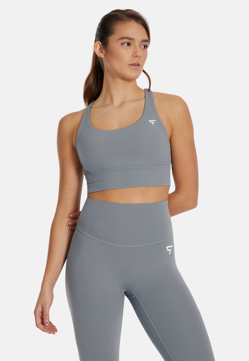 Sostenedor deportivo gris y leggings de tiro alto a juego, fabricados con un tejido suave, que presentan un diseño minimalista con acentos de logotipo blanco.