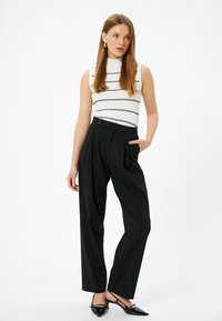 Biała bezrękawnikowa bluzka w czarne paski zestawiona z czarnymi spodniami o wysokim stanie. Spodnie mają z przodu kanty i kieszenie boczne. Czarne buty.