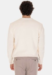 Maglione lavorato a maglia color crema con scollo rotondo e polsini a coste. Il design presenta una finitura testurizzata e una vestibilità rilassata.