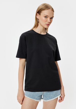 Sort bomulds T-shirt med rund halsudskæring og korte ærmer, sammen med lyse denimshorts med frynset kant.
