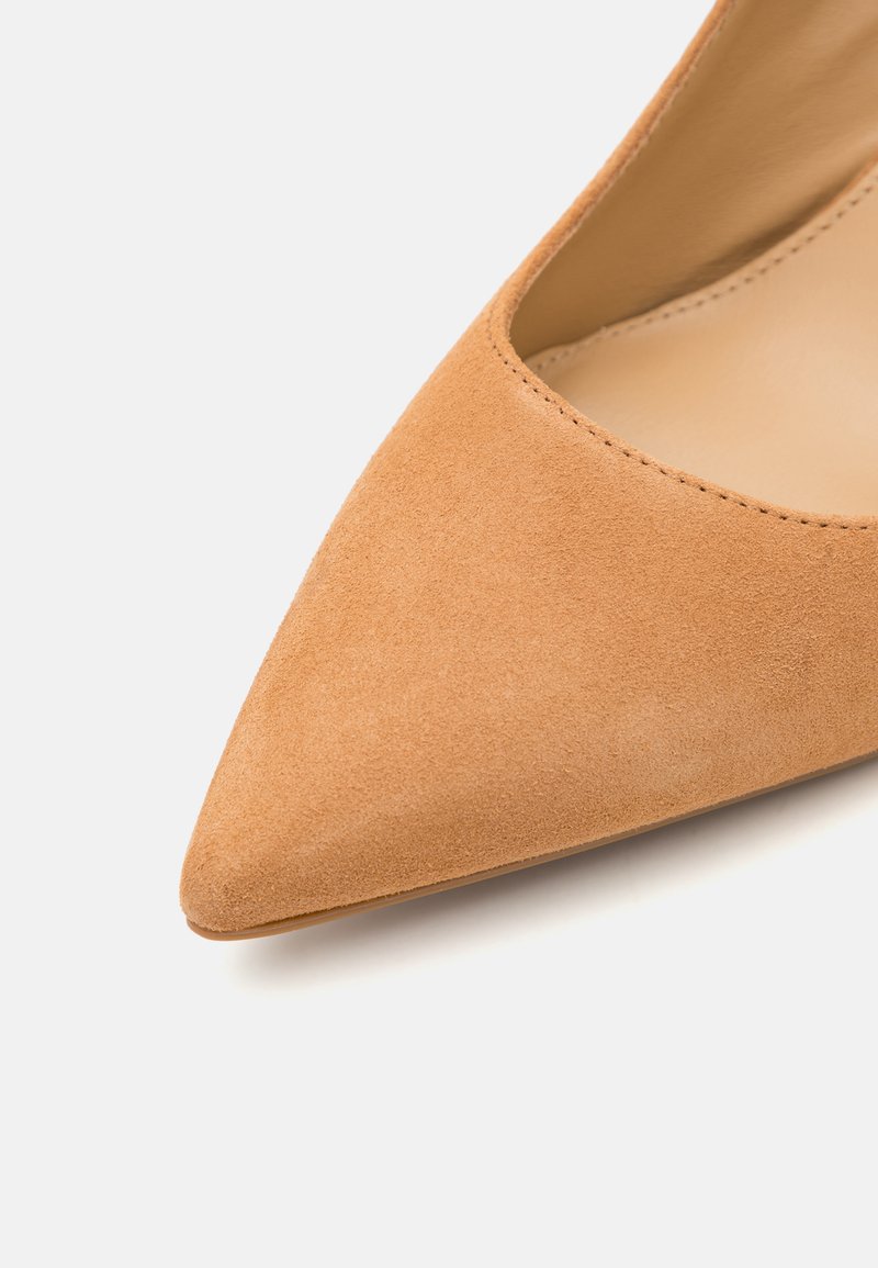 Chaussure à talon haut en suède tan avec un bout pointu et une partie supérieure ouverte. Présente une texture lisse et des coutures propres le long des bordures.