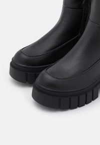 Schwarze Knöchelstiefel aus glattem Leder mit einer robusten Gummiplattformsohle und seitlichem Reißverschluss. Runde Zehenform und sichtbare Nahtdetails.