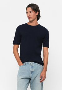 Navy blue short-sleeve t-shirt in a soft material with a round neckline. Worn with light blue denim jeans, featuring a classic fit.