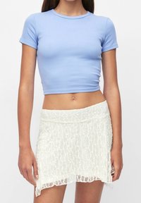 Světle modrý přiléhavý top s krátkými rukávy v kombinaci s bílou krajkovou mini sukni s vlnitými okraji a texturovaným květinovým vzorem.