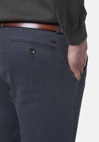 Mörkgrå byxor i texturerad tyg med sidoficka och bälteshällor, utrustade med ett brunt läderbälte och en knappdetalj på baksidan.