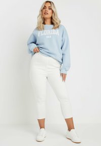Sudadera azul claro con el texto "FLORIDA USA", combinada con jeans blancos ajustados y zapatillas blancas. Tejido suave, corte relajado y longitud hasta el tobillo.