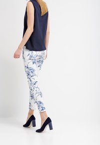 Sjöblå ärmlös topp i kombination med vita blommiga slim-fit byxor och sjöblå högklackade skor med blockklack. Svala och mjuka tygtexturer.