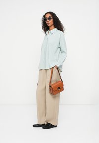 Light blue, long-sleeve shirt with a collar and textured pattern, paired with beige wide-leg pants and a small brown handbag. Black shoes.
