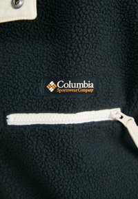 Pullover in pile Columbia di colore nero con una tasca con zip color crema. Presenta una superficie testurizzata e un'etichetta con logo arancione.