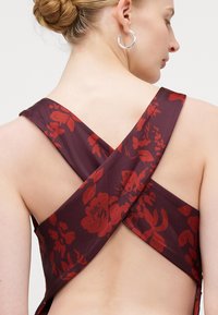Rochie bordeaux cu un model floral în roșu, având un design cu spate încrucișat și bretele late. Material neted cu un luciu delicat.