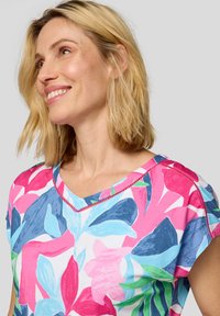 Mehrfarbiges Blumenbluse mit V-Ausschnitt und kurzen Ärmeln. Das Design umfasst blaue, rosa und grüne Blätter auf einem weißen Hintergrund.