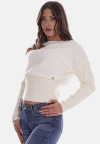 Maglione corto bianco con la parte superiore testurizzata e la parte inferiore a coste. Presenta un piccolo dettaglio del logo e maniche lunghe. Abbinato a jeans blu.