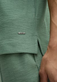 Top in tessuto verde menta con una etichetta in argento del logo JOOP! sull'orlo. Il design presenta una vestibilità comoda e dettagli cuciti visibili.