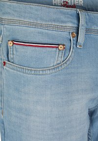 Light blue denim jeans with a classic cut. Features a front pocket with gold hardware and a tricolor striped accent. Subtle stitching detail.