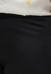 Κοντινό πλάνο μαύρης υφασμάτινης φούστας σε συνδυασμό με λευκό υφασμάτινο πουκάμισο με κίτρινη λουλουδένια κεντητική.