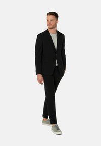 Zwart colbert over een lichtgrijs T-shirt, gecombineerd met zwarte broek en grijze sneakers. Kenmerkt zich door een slim fit en minimalistisch ontwerp.