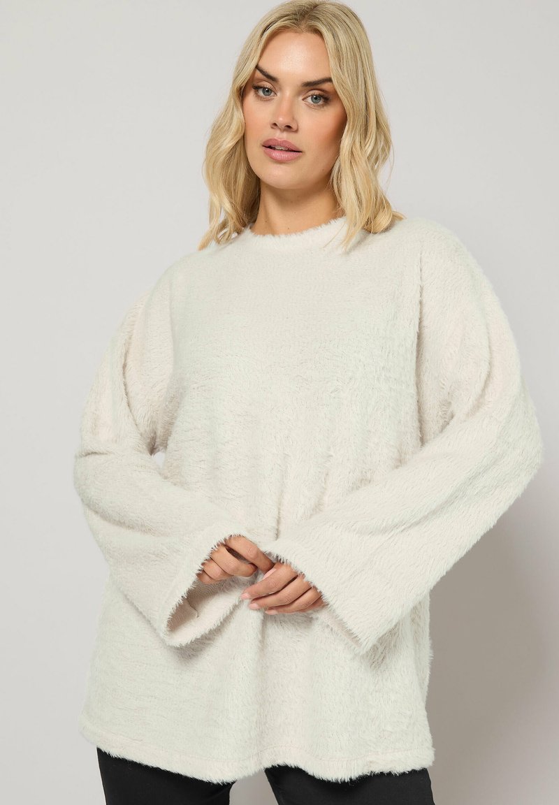 Haut à manches longues, moelleux et de couleur crème, avec une coupe décontractée et des manches larges. Le tissu texturé a un aspect doux et duveteux.