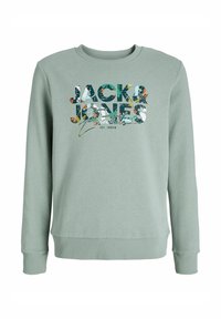 Sweatshirt vert clair à manches longues, poignets et ourlet côtelés. Présente un imprimé graphique multicolore de "JACK & JONES" sur la poitrine.