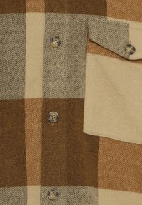 Primo piano di tessuto a quadri marrone e beige con bottoni e tasca a patta su un capo di lana.