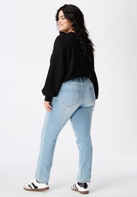 Sweat-shirt noir court avec des manches bouffantes, associé à un jean bleu clair à coupe décontractée et des baskets blanches avec des rayures noires.