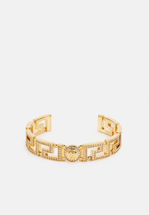 Gold cuff bracelet featuring geometric cutouts, embellished with rhinestones, and a central medallion detail. Smooth metal texture.