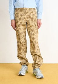Beige camo cargo bukser med et struktureret stof, der har sidelommer og elastiske manchetter; båret med grå og sølv sneakers.
