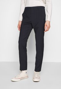 Námořnické kostkované kalhoty se slim fit a texturovanou tkaninou. Obsahují boční kapsy a poutka na opasek. V kombinaci s béžovými vysokými teniskami.