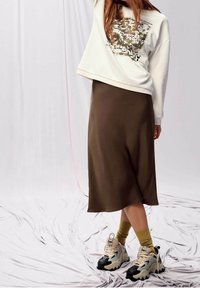 Sudadera blanca con diseño gráfico, combinada con una falda midi marrón. El calzado incluye zapatillas de deporte gruesas en negro y beige con calcetines amarillos.