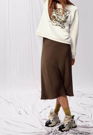 White sweatshirt with graphic design, paired with a brown midi skirt. Footwear includes chunky black and beige sneakers with yellow socks.