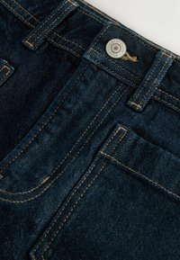 Donkerblauwe denim jeans met een knoopsluiting, voorzakken met contrasterende gouden stiksel en een zachte textuur.