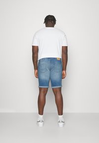 Kort denimshorts i ljusblått, med uppvikta kanter, bakfickor och en ljusbrun läderlapp vid midjan. Bärs med en vit t-shirt.