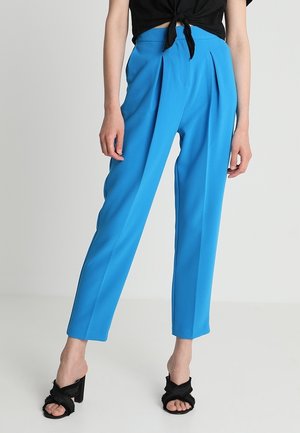 Woman wearing bright blue high-waisted tailored pants paired with black heeled sandals and a black tied crop top.