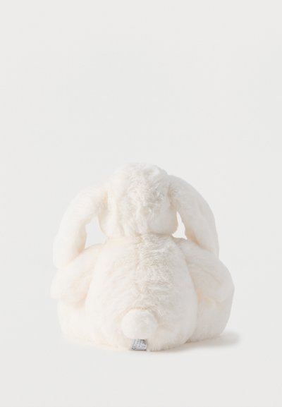 Λευκό παιχνιδάκι κουνελάκι από μαλακό βελούδινο υλικό, καθιστό με την πλάτη προς τα εμάς, δείχνει τα πεσμένα αυτιά, την αφράτη ουρά και την ετικέτα ύφασμα στο κάτω κέντρο.